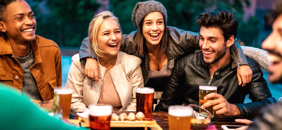 A group of friends is smiling and having a good time while sitting at a restaurant and drinking beer