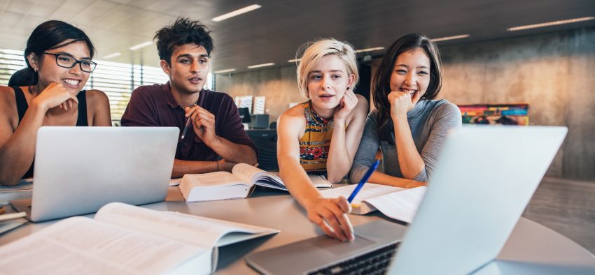 College students using laptop while sitting at table. Group study for school assignment.