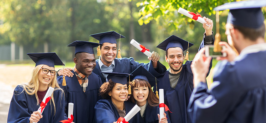 Group of young people with diplomas and graduation hats posing and smiling for group photo