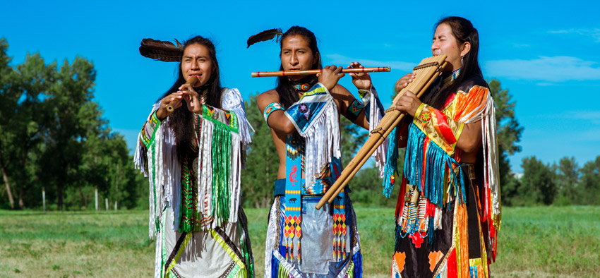 Three native Americans playing flute and wearing traditional clothes on a sunny day