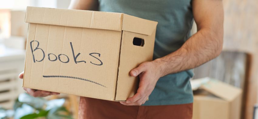 Close-up of man holding cardboard box with books while moving the house