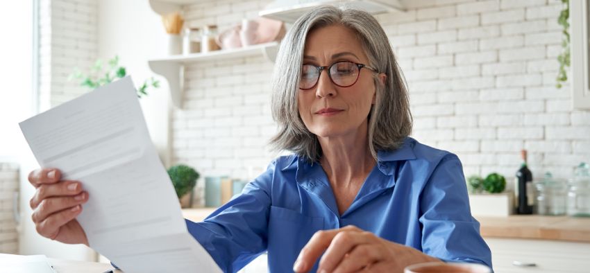 Senior mature business woman holding paper bill using calculator, old lady managing account finance, calculating money budget tax, planning banking loan debt pension payment sit at home kitchen table.