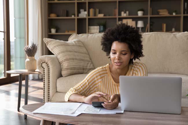 African-american woman makes calculations on calculator pay utility bills, loan via e-bank application on computer. sit in living room alone. Personal family budget management, modern tech, accounting concept
