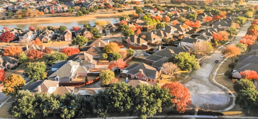 Aerial view waterfront residential subdivision with cul-de-sac dead-end street in suburban Dallas, Texas. Urban sprawl with row of single-family houses and colorful fall leaves, blue sky