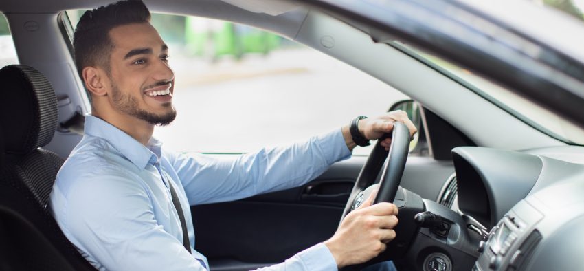 Excited arab guy going to office in the morning, driving his car, side view, copy space. Cheerful middle-eastern young man looking at the road, sitting inside luxury automobile, going home from job