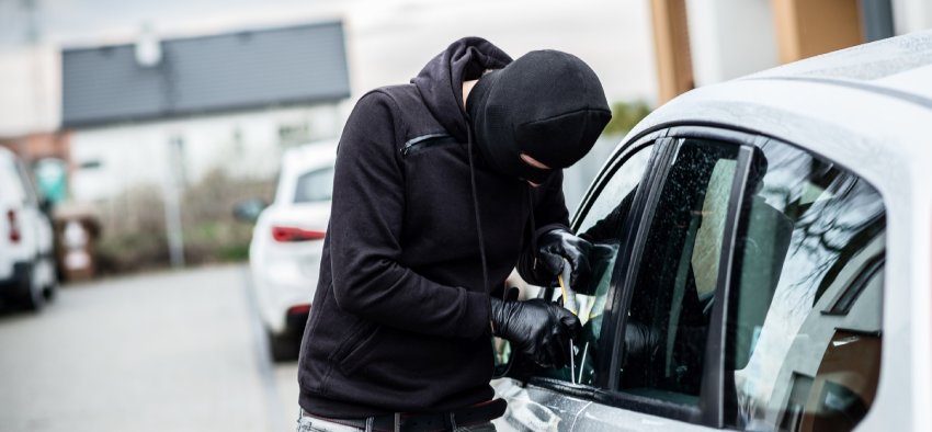 Car thief trying to break into a car with a screwdriver. Car thief, car theft.