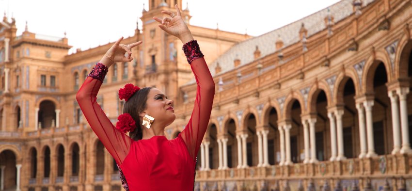 Beautiful teenage woman dancing flamenco in a square in Seville, Spain. She wears a red dress with ruffles and dances flamenco with a lot of art. Flamenco cultural heritage of humanity.