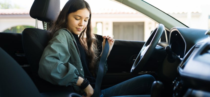 Teenage girl putting on her safety seatbelt and about to start the car. Teen driver getting ready to drive her new car