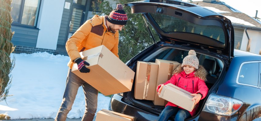 Father and daughter moving to new apartment together during winter standing outdoors near car taking boxes from trunk looking camera smiling excited