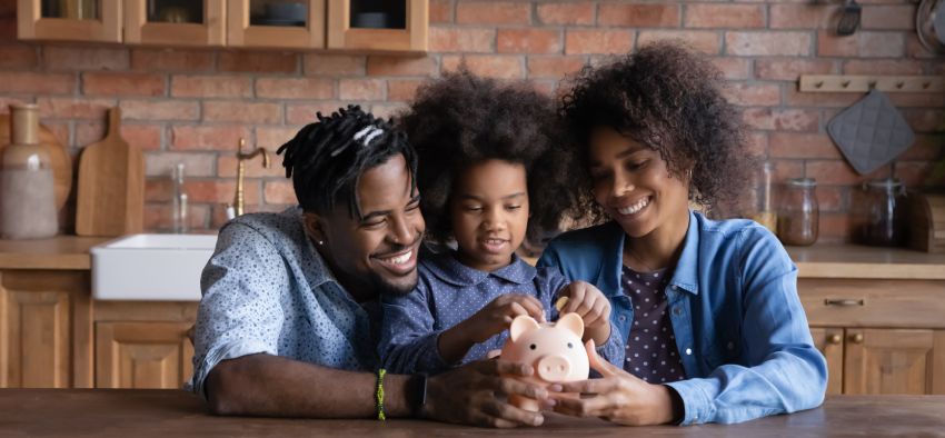 Smiling young African American family with daughter save money in piggybank feel provident economical about finances. Happy biracial parents with ethnic child make financial investment for future.