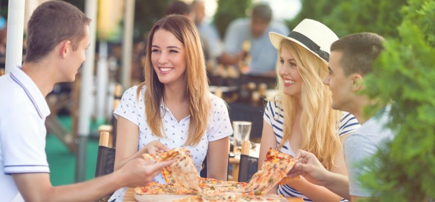 Four cheerful young friends sharing pizza in a outdoor cafe
