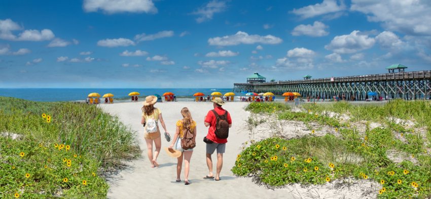 Family relaxing on the beautiful beach, People enjoying summer vacation by the ocean. Family walking on the beach. Cloudy sky and pier in the background. Folly Beach, South Carolina USA.