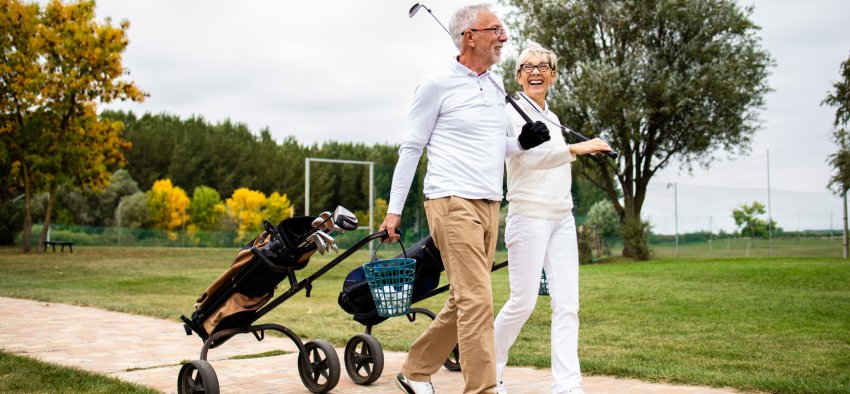 An elegant senior couple enjoying free time in retirement by playing golf and walking to the practice range.