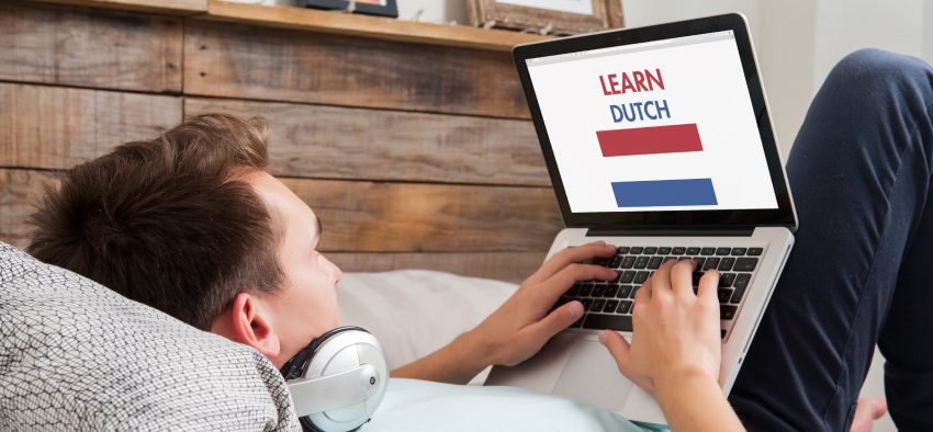 Man learning dutch language with a laptop computer lying down on the bed at home