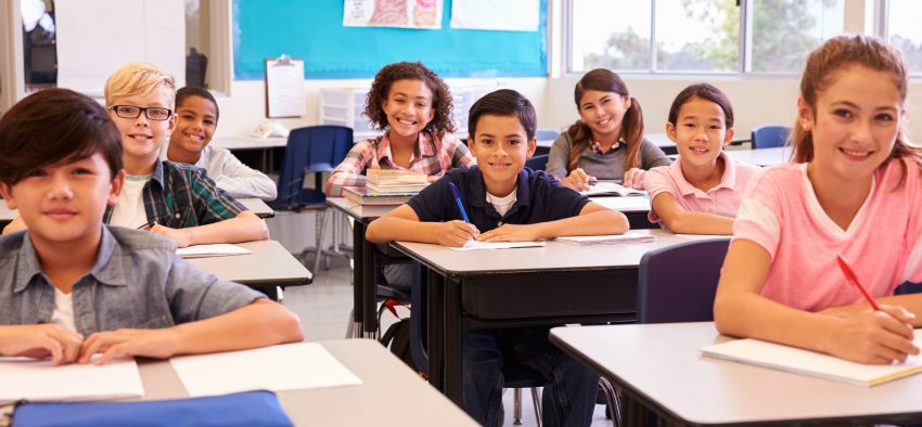 Smiling elementary school kids sitting at desks in classroom