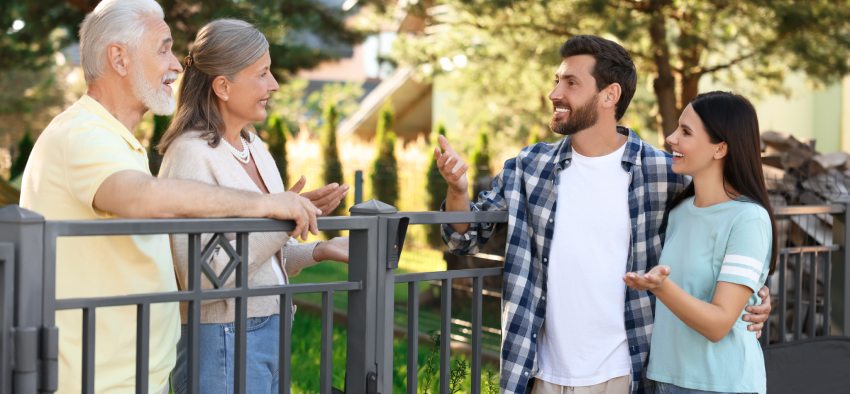 Friendly relationship with neighbours. Young family talking to elderly couple near fence outdoors