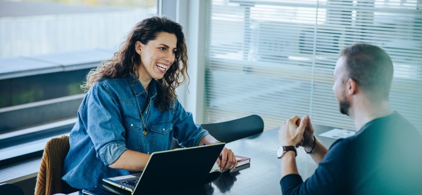 Smiling businesswoman taking interview of a job applicant. Friendly recruitment manager interviewing young man in office boardroom.