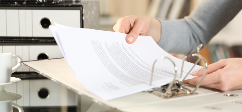 Close up of woman hands organizing documents putting files on folder on a desk at home